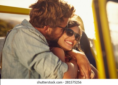 Young man embracing and kissing his beautiful girlfriend while on a road trip. Romantic couple in a car on summer holiday.