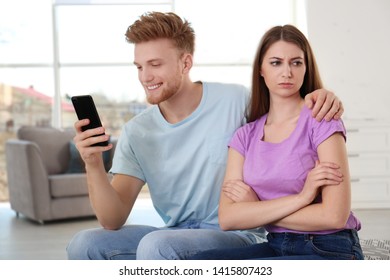 Young man engaged in smartphone while spending time with his girlfriend at home. Loneliness concept