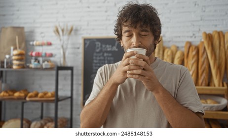 Young man enjoying coffee in an indoor bakery surrounded by bread and pastries - Powered by Shutterstock