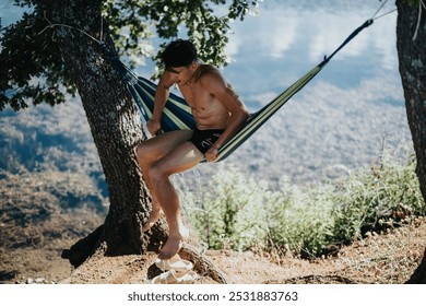 Young man enjoying a peaceful moment in a hammock by the lakeside on a sunny summer day with nature all around. - Powered by Shutterstock