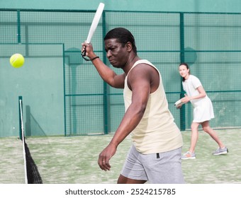 Young man enjoying popular racket sport padel, playing doubles game with female friend on court outdoor - Powered by Shutterstock