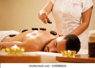 Young man enjoying in relaxing hot stone therapy during spa treatment. 