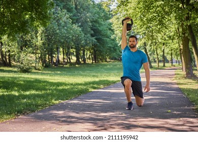 Young Man Exercises Kettlebell Lunges During A Workout Outside In A Park During Sunny Summer Day