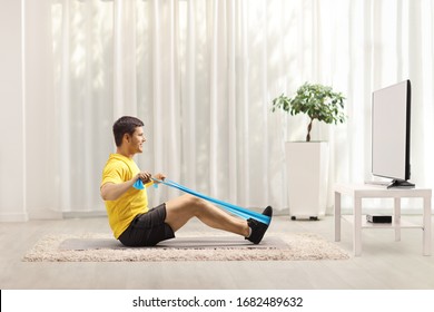 Young man exercising with an elastic band in front of a TV at home