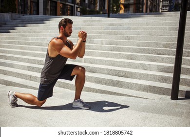 Young Man Exercising Outside. Strong Powerful Guy Stand On One Knee And Hold Hands In Front Himself. Doing One Leg Squat Exercise. Training His Body And Muscles.