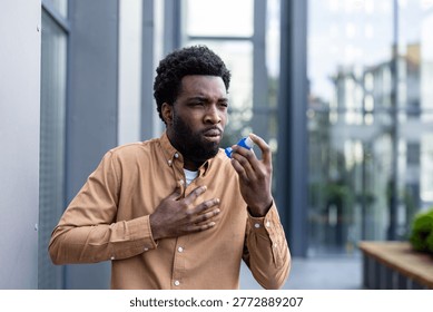 Young man experiencing an asthma attack and difficulty breathing, using an inhaler to alleviate chest pain and respiratory distress in an urban outdoor setting