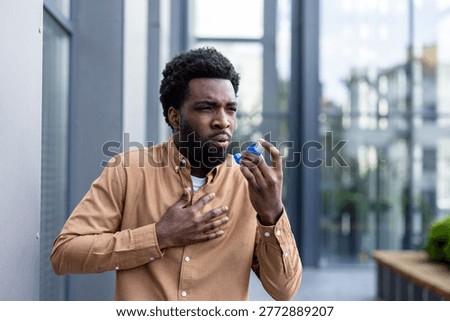 Young man experiencing an asthma attack and difficulty breathing, using an inhaler to alleviate chest pain and respiratory distress in an urban outdoor setting