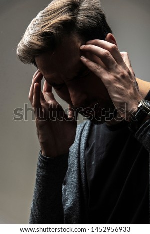 Young man experiencing throbbing headache and pain, studio image, gray background