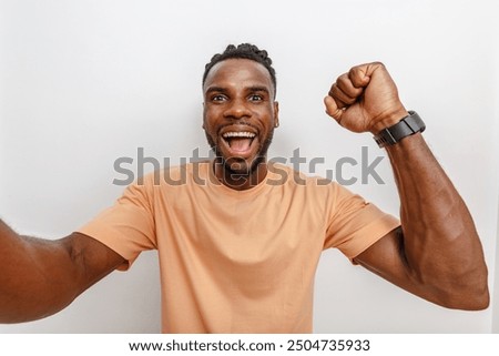 Cheerful man celebrating his success with a broad smile and raised fist in front of a neutral background