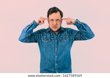 Young man with expression of concentration. Denim shirt and isolated Pastel pink background.