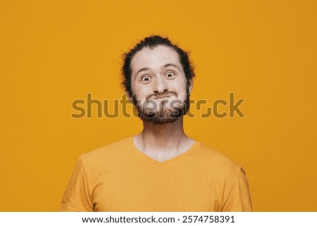 Young man with an expressive face making a funny grimace in a vibrant orange t shirt against a bold yellow background, showcasing joy and playfulness
