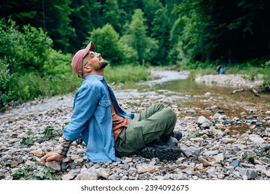 Young man with eyes closed relaxing by the creek while hiking in nature. - Powered by Shutterstock