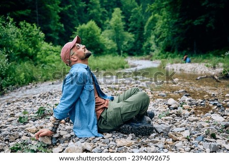 Young man with eyes closed relaxing by the creek while hiking in nature.