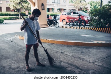 A Young Man In A Face Mask Does Community Work At A Mall, Using A Walis Tingting Or A Local Broom To Clean The Concrete.