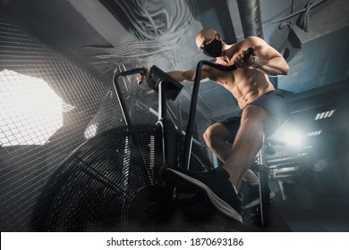 Young Man in Face Mask doing Exercise on Spin Bike in dark Fitness Gym. Guy Riding on Spinning Bike. Training during self-isolation COVID. Healthy Lifestyle and Sport Concepts. Functional training. - Shutterstock ID 1870693186