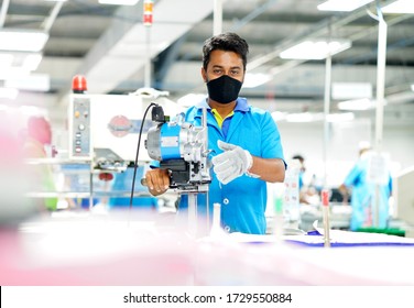 Young man in a face mask and protective chain gloves at work. Man with cutter machine and personal protective equipment at garment industrial work place. Fabric cutter in Asian textile garment factory