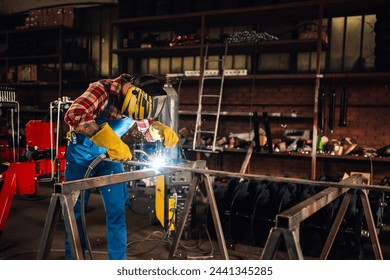 Young man in a factory welding metal with welding machine while wearing a protective gear. Yellow sparks flying in sides during working with steel at workshop. Dangerous work concept. Copy space. - Powered by Shutterstock