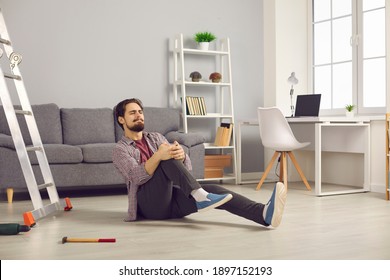 Young Man Fallen From Ladder Sitting On Floor And Suffering From Awful Pain. Unlucky Guy Fell Off Ladder While Doing Home Repairs And Hurt His Knee. Concept Of Dangerous Domestic Accidents