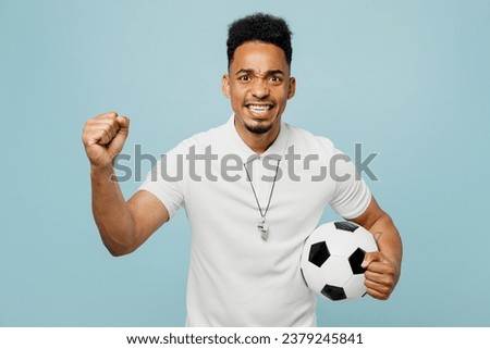Young man fan wear basic t-shirt whistle cheer up support football sport team hold in hand soccer ball watch tv live stream motivating do winner gesture isolated on plain pastel blue color background