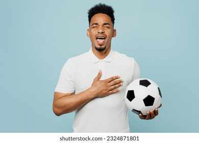 Young man fan wearing basic t-shirt sing national country anthem cheer up support football sport team holding in hand soccer ball watch tv live stream isolated on plain blue color background studio