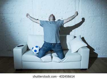 Young Man Fanatic And Crazy Football Fan Watching Television Soccer Match Alone Screaming Happy Celebrating Scoring Goal In Glad In Ecstasy With Ball On Home Couch