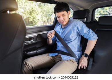 young man fastening a seat belt while sitting in the back seat of car 