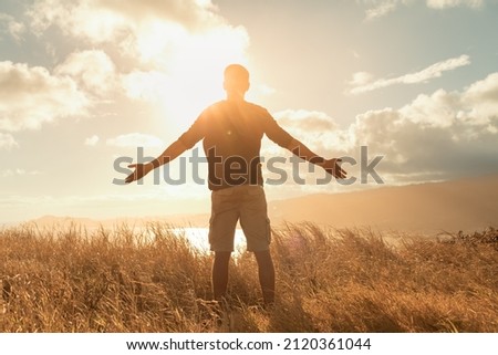 Young man feeing happy outdoors standing on a mountain taking in the warm rays of sunshine. Freedom, and happiness concept. 