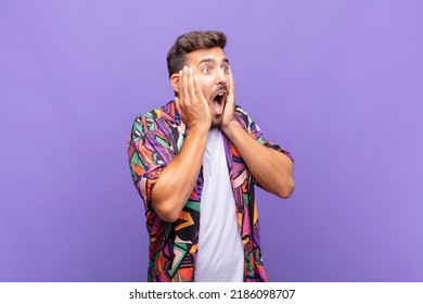 young man feeling happy, excited and surprised, looking to the side with both hands on face