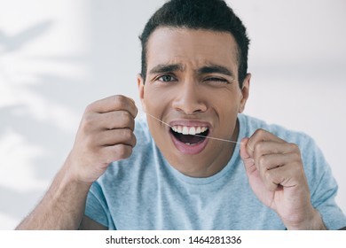 Young Man Feeling Pain While Using Dental Floss And Looking At Camera