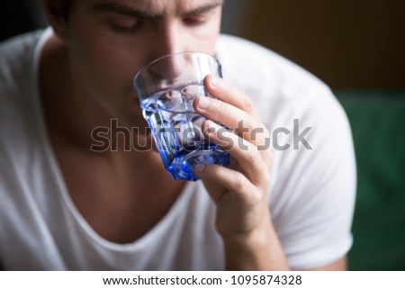 Young man feeling thirsty dehydrated holding glass drinking pure mineral fresh water for body refreshment and energy recovery, dehydration problem or water filters delivery concept, close up view