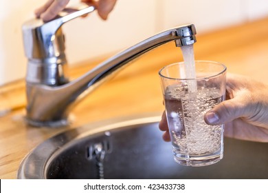 Young Man Filling Up A Glass With Water In The Sink In Kitchen At Home.