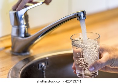 Young Man Filling Up A Glass With Water In The Sink In Kitchen At Home.