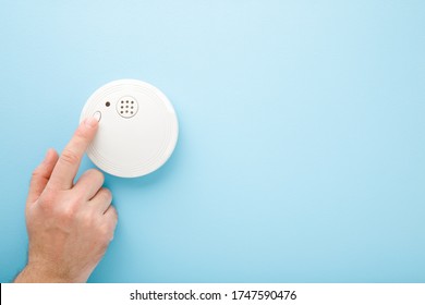 Young Man Finger Touching New White Plastic Smoke Alarm. Light Blue Table Background. Pastel Color. Safety Concept. Empty Place For Text.