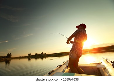 Young Man Fishing From A Boat At Sunset