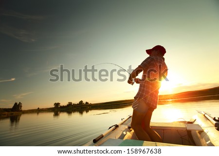 Young man fishing from a boat at sunset
