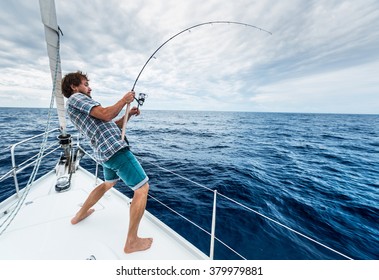 Young man fishing hard in open sea from sail boat