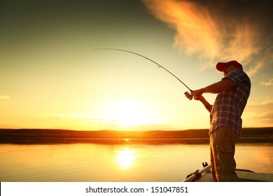 Young man fishing on a lake from the boat at sunset - Powered by Shutterstock