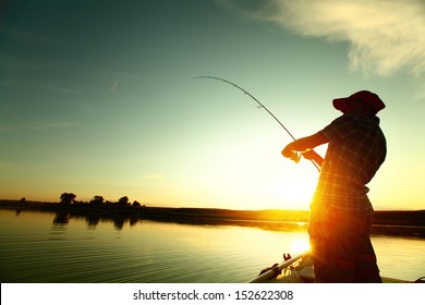 Young man fishing on a lake from the boat at sunset