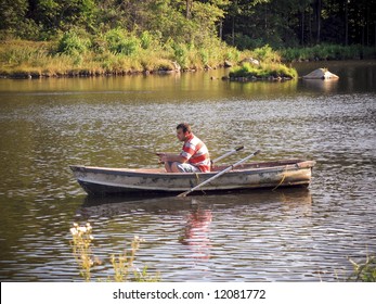 A Young Man Fishing Out Of A Row Boat.