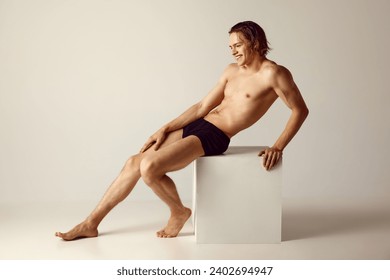 Young man with fit, muscular body sitting shirtless in underwear against grey studio background. Concept of men's beauty, health, body care, sportive lifestyle. Empty space to insert text - Powered by Shutterstock