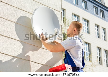 Young Man Fitting TV Satellite Dish To Wall