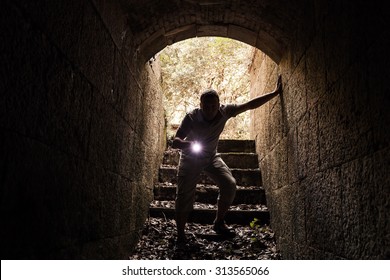 Young Man With A Flashlight Enters The Stone Tunnel And Looks In The Dark, Warm Tonal Correction Photo Filter Effect