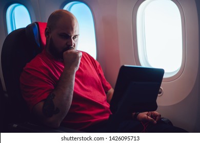 Young Man Flight Passenger Watching Movie On Board Via Entertainment Tv While Sitting In Comfortable Airplane Seat Next To Aircraft Cabin Window. Caucasian Man Enjoying Travel Via Business Class