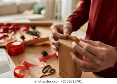 The young man is focused on wrapping a Christmas gift, showcasing his holiday spirit and creativity. - Powered by Shutterstock