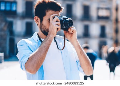 Young man focusing to make cool photos on vintage camera during summer travel in old architectural city.Professional photographer dressed in casual outfit taking pictures standing in downtown - Powered by Shutterstock