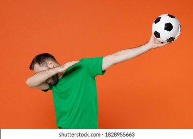 Young Man Football Fan In Green T-shirt Cheer Up Support Favorite Team With Soccer Ball Doing Dab Hip Hop Dance Gesture Hiding Cover Face Isolated On Orange Background. People Sport Leisure Concept