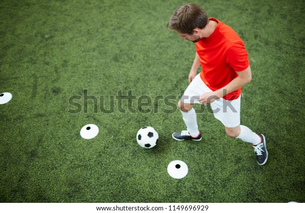 Young man in football uniform running\
after soccer ball by dividing line on green\
field