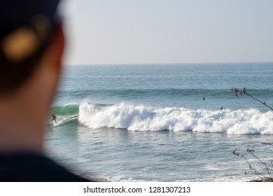 A Young Man In The Foreground Checking The Swell While A Surfer Is Catching A Wave At Iconic Anchor Point, The Most Famous Surf Spot In Morocco. 