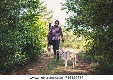 Young man in the forest with husky dogs and guitar bag 
