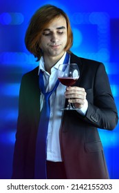 A Young Man In A Formal Suit With A Tie Holds A Glass Of Wine At An Office Party Or Prom. A 21 Year Old Guy Drinks Alcohol.